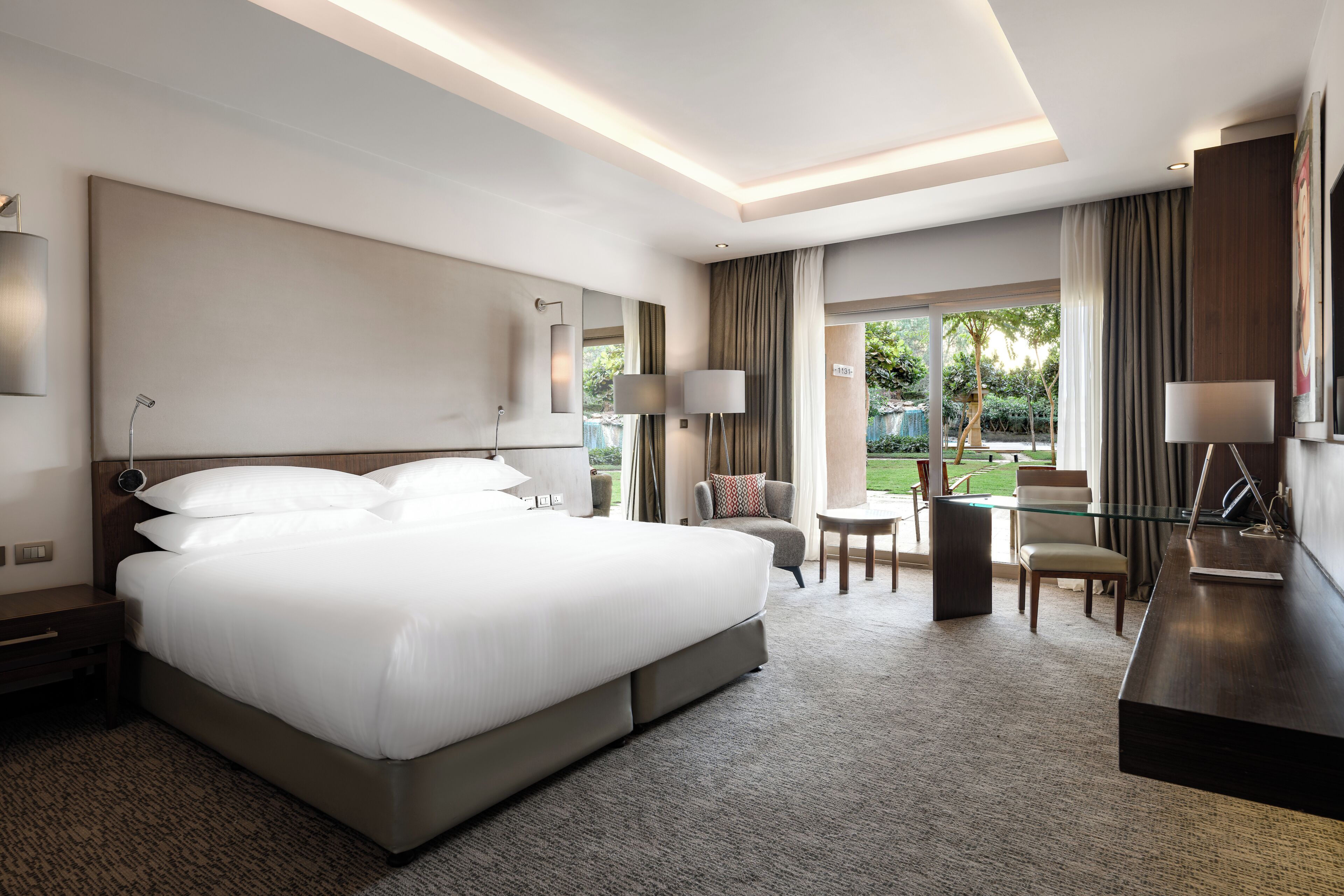 Una habitación de hotel moderna con una cama grande, un escritorio y vistas al jardín.