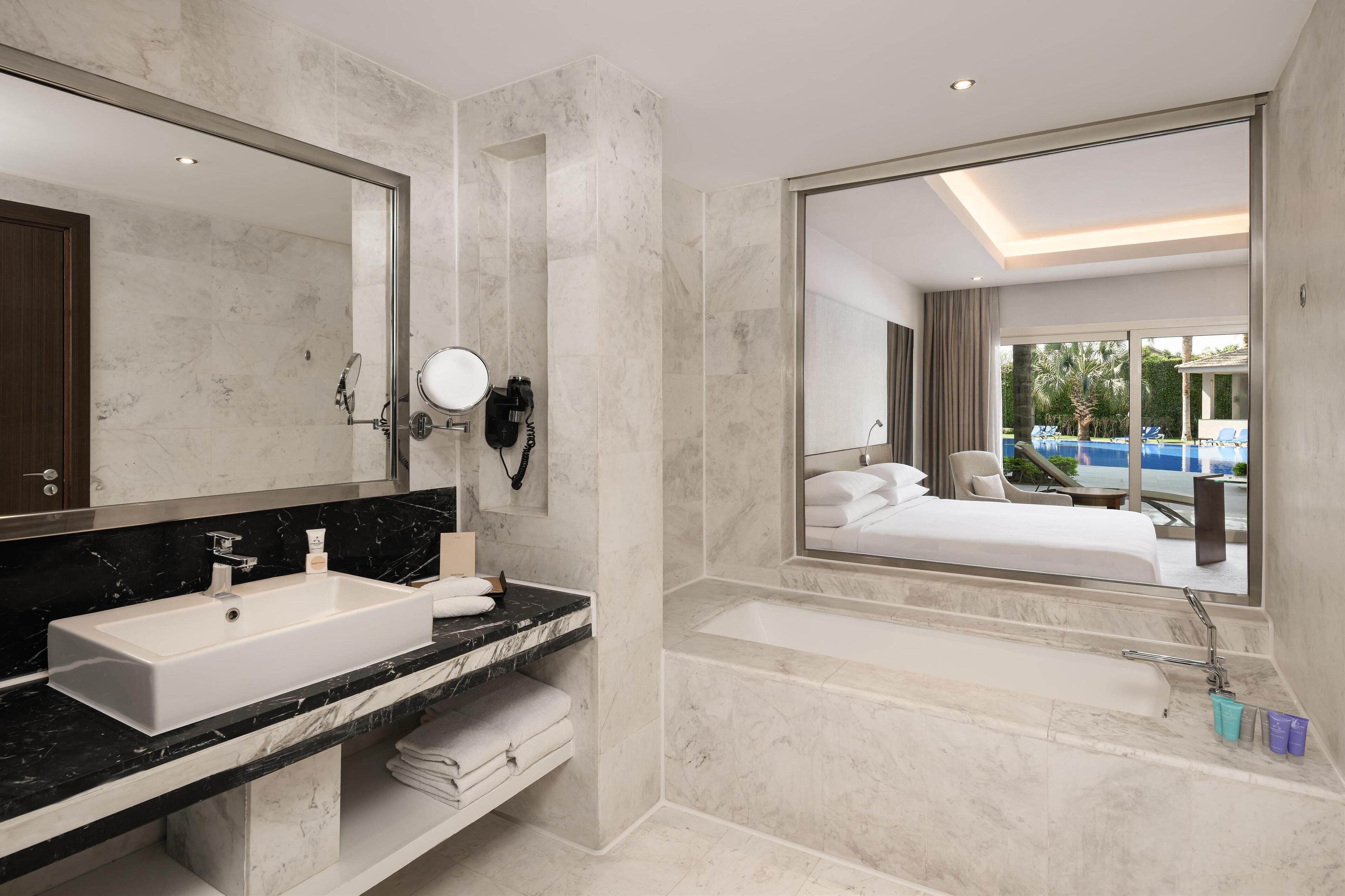 Un baño de hotel moderno con un espejo grande, un lavamanos, una bañera y una ducha.