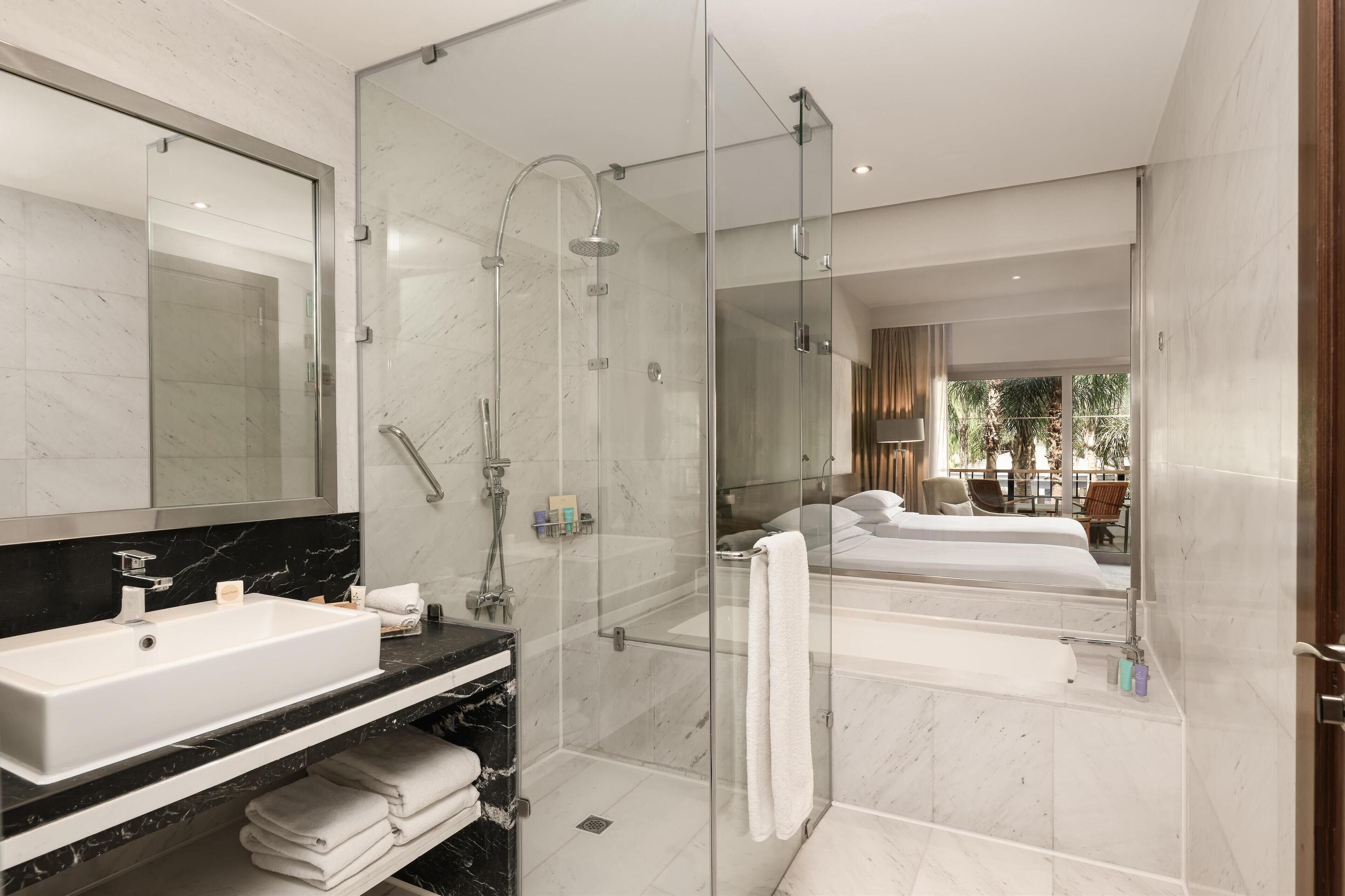 Un baño moderno con ducha de vidrio, un espejo grande, un lavamanos blanco y una bañera.
