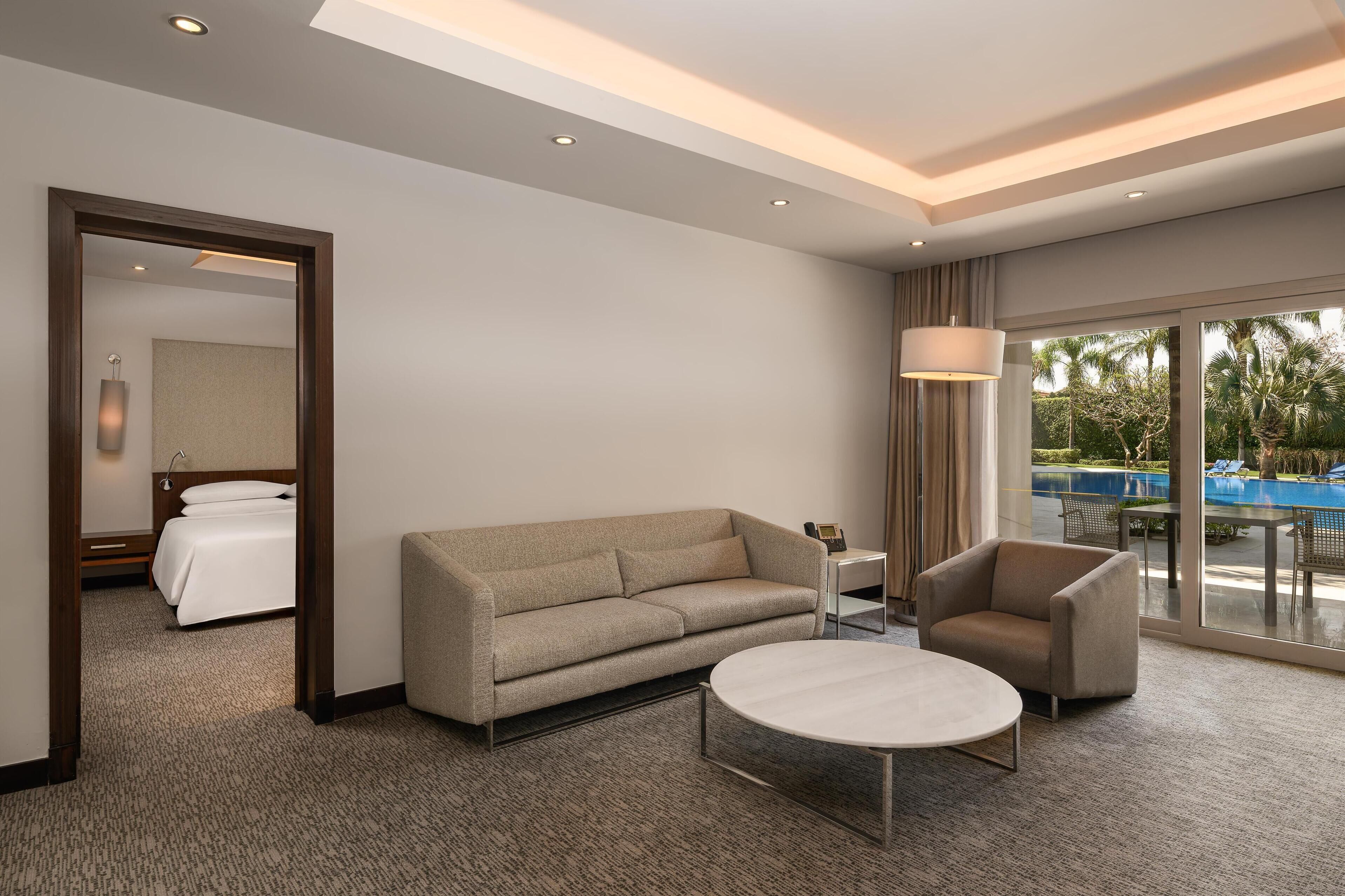 Una habitación de hotel moderna con cama, sofá, mesa de centro y vista a una piscina.