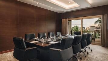 Une salle de conférence avec une longue table, des chaises noires et une vue sur les palmiers, visible à travers de grandes fenêtres.