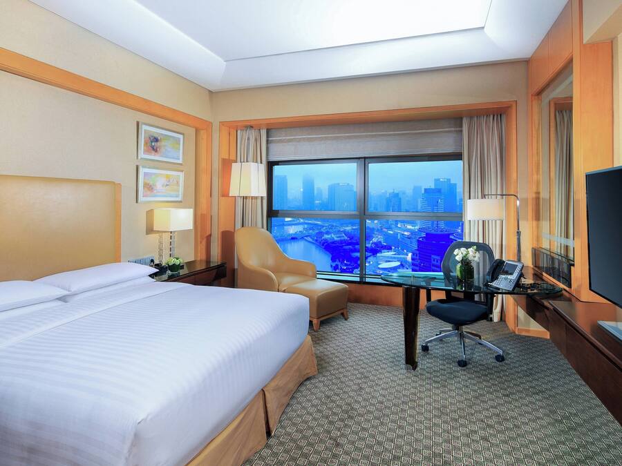 Quarto de hotel com uma cama grande, uma mesa com computador, uma cadeira e uma TV.