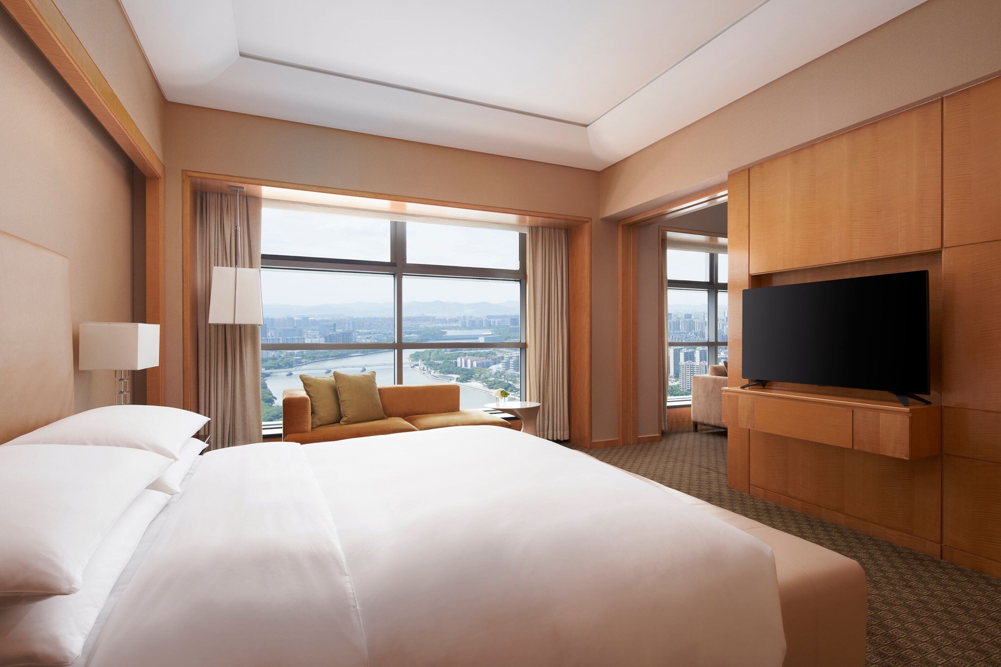 Habitación de hotel con una cama grande, un sofá, un televisor y vistas a la ciudad.