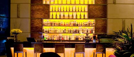 A bar area with multiple shelves of bottles, bar stools, and a round table with a glass.