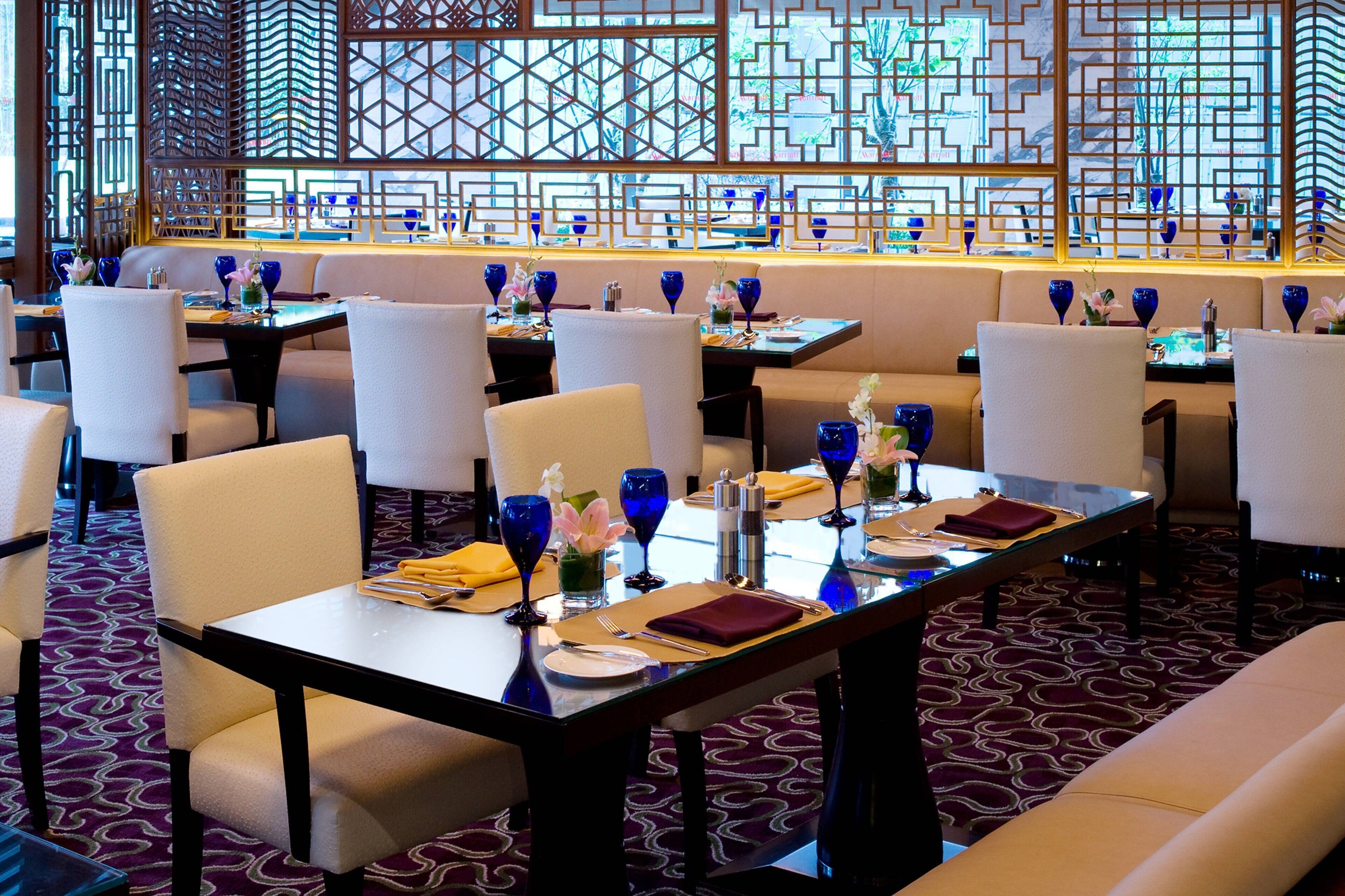 Ein Restaurant mit mehreren gedeckten Tischen, einem gemusterten Teppich und einer dekorativen Trennwand mit geometrischen Mustern.