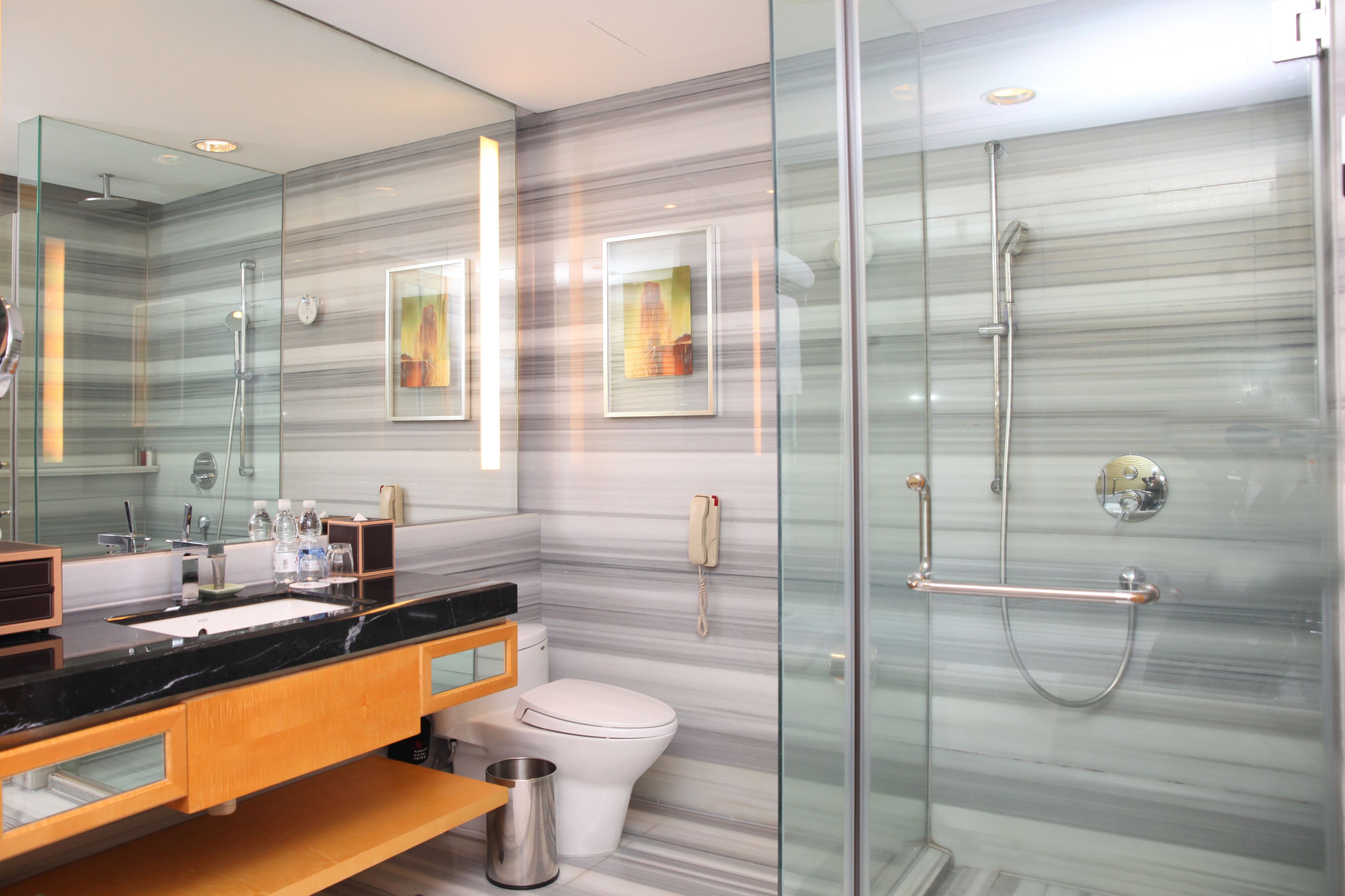A modern bathroom with a glass shower enclosure, a marble backsplash, and a wooden vanity.