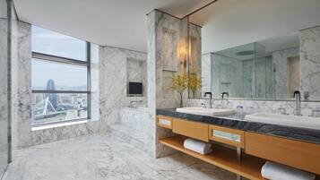 Un baño moderno con paredes de mármol, un ventanal grande, lavamanos dobles y cabina de ducha de vidrio.