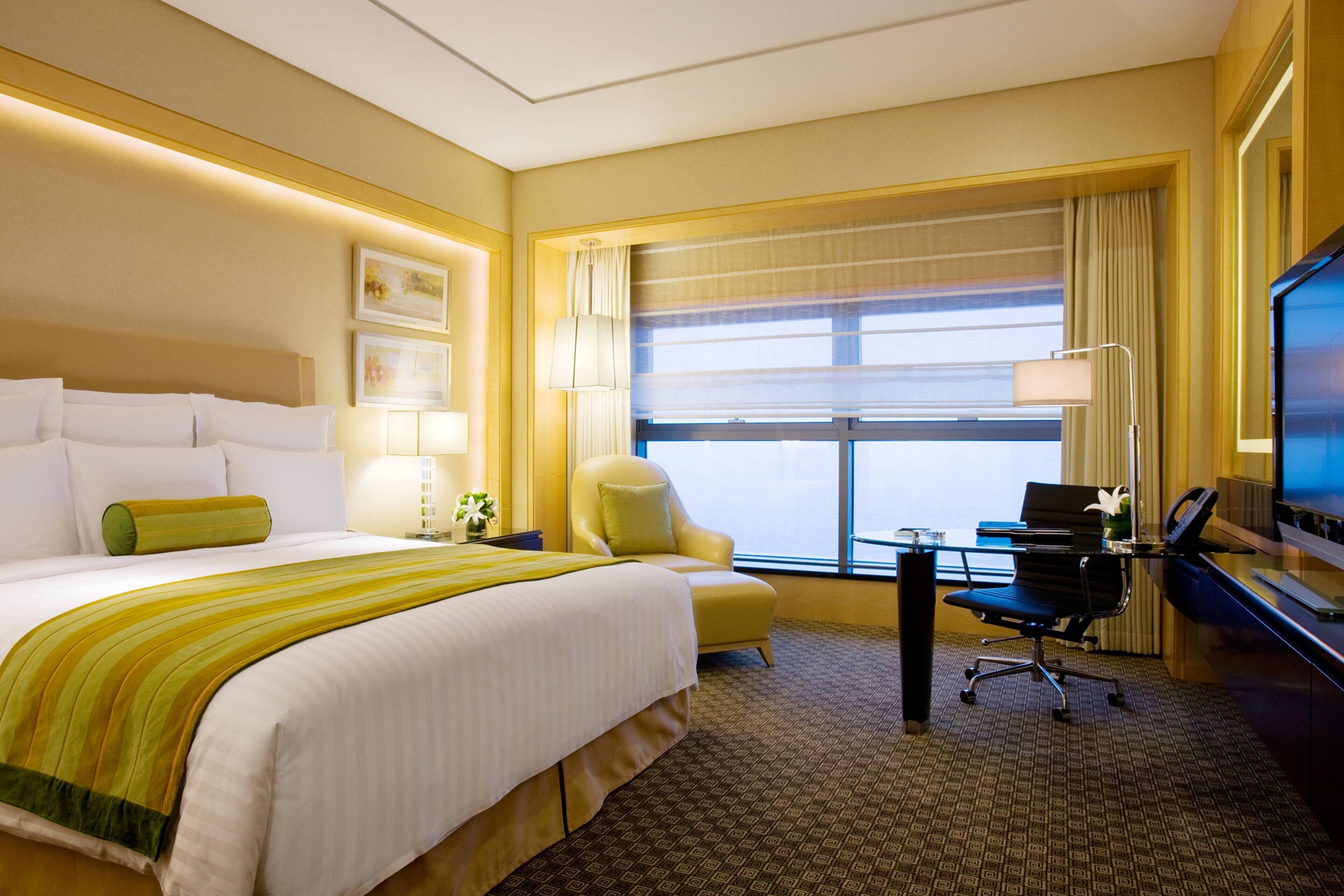 A hotel room with a large bed, a desk with a computer, a chair, and a TV.
