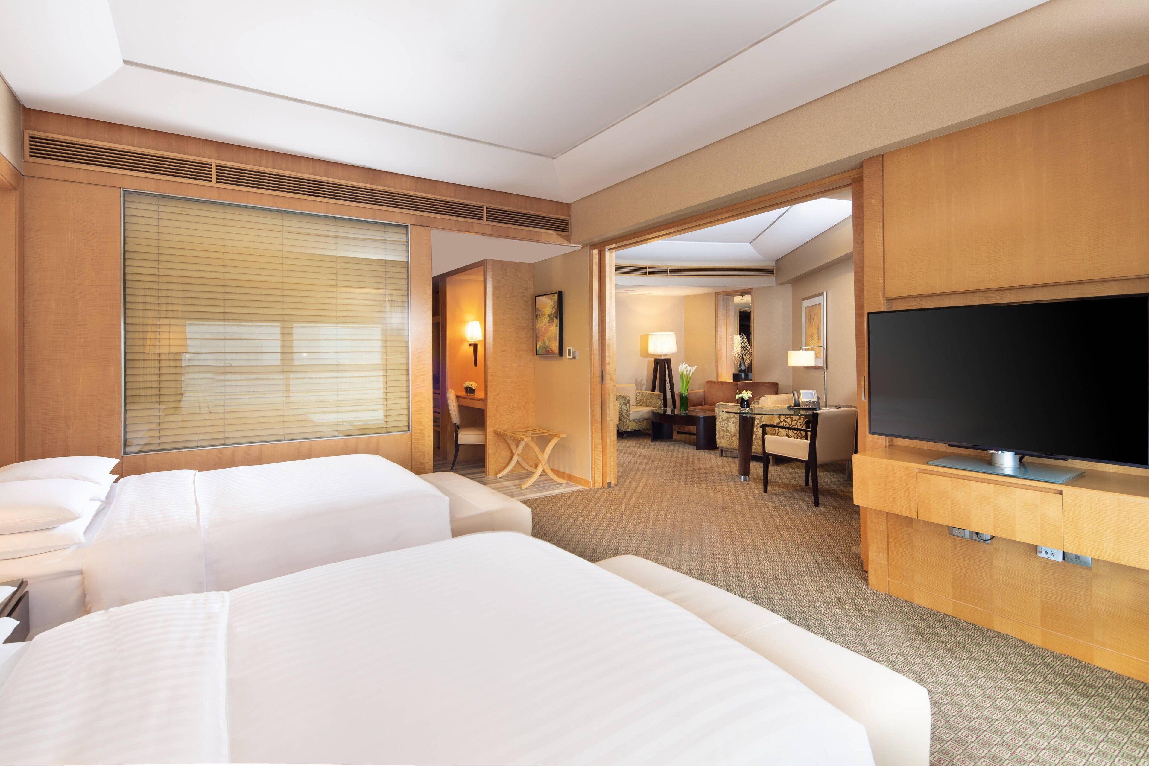 A hotel room with two beds, a television, a desk, and a seating area with a lamp.