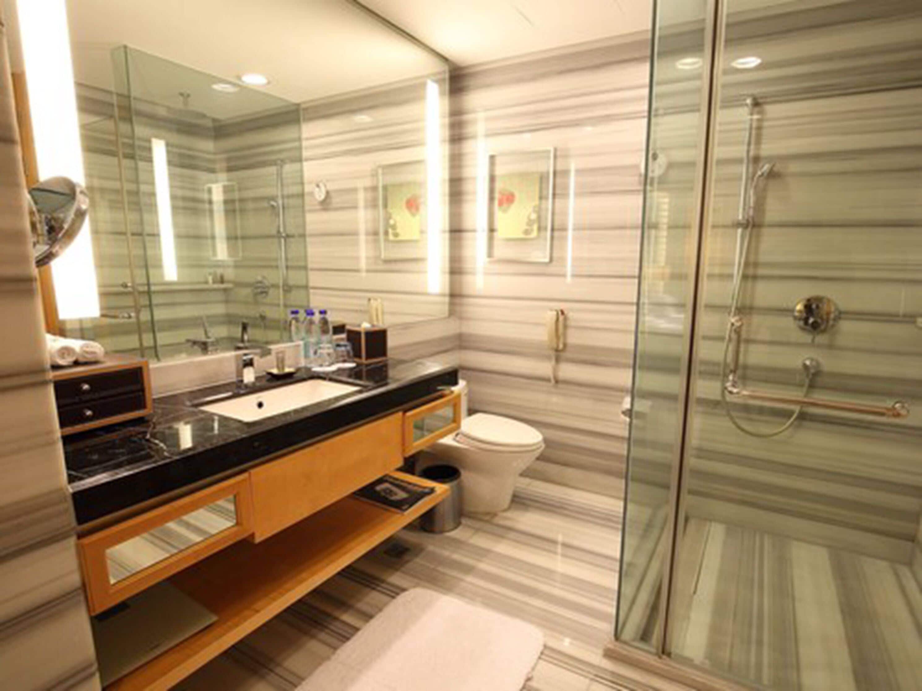 A modern bathroom with a glass shower enclosure, a marble vanity, and a large mirror.