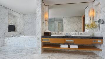 Un baño moderno con suelo de mármol, un lavabo grande, un espejo y un televisor instalado en la pared.