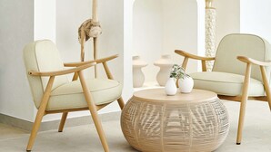 A modern interior with a white wall, a wooden floor, two light-colored chairs, a round wicker table, and a shelf with decorative items. - Iberostar Selection Albufera Park - All Inclusive (Muro)