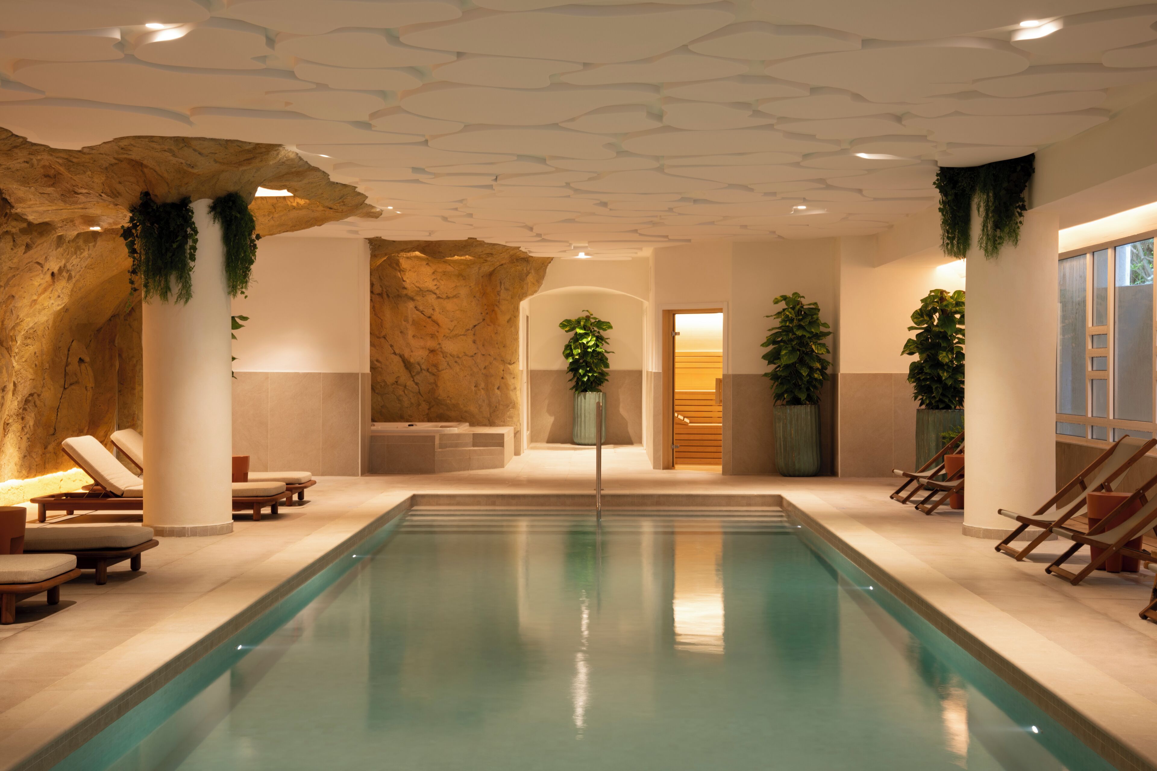 Una piscina con sillas de descanso, una pared de roca y plantas en macetas.