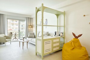 A modern hotel room with a green console bed, a yellow bean bag, a white sofa, and a dining table.