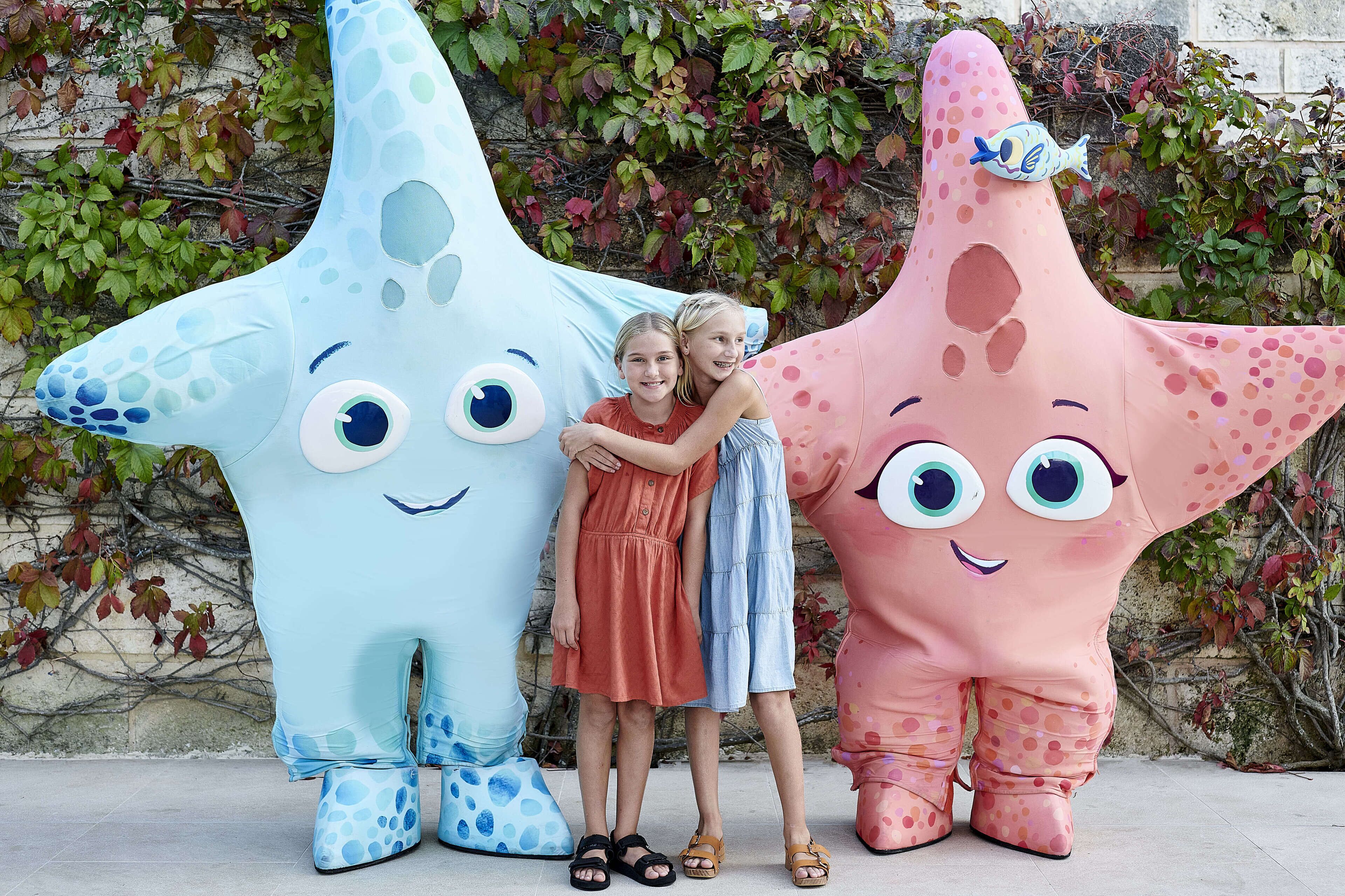 Dos niños abrazando grandes figuras inflables de estrella de mar.