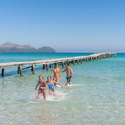 A pier extending into clear turquoise water with a mountainous backdrop.