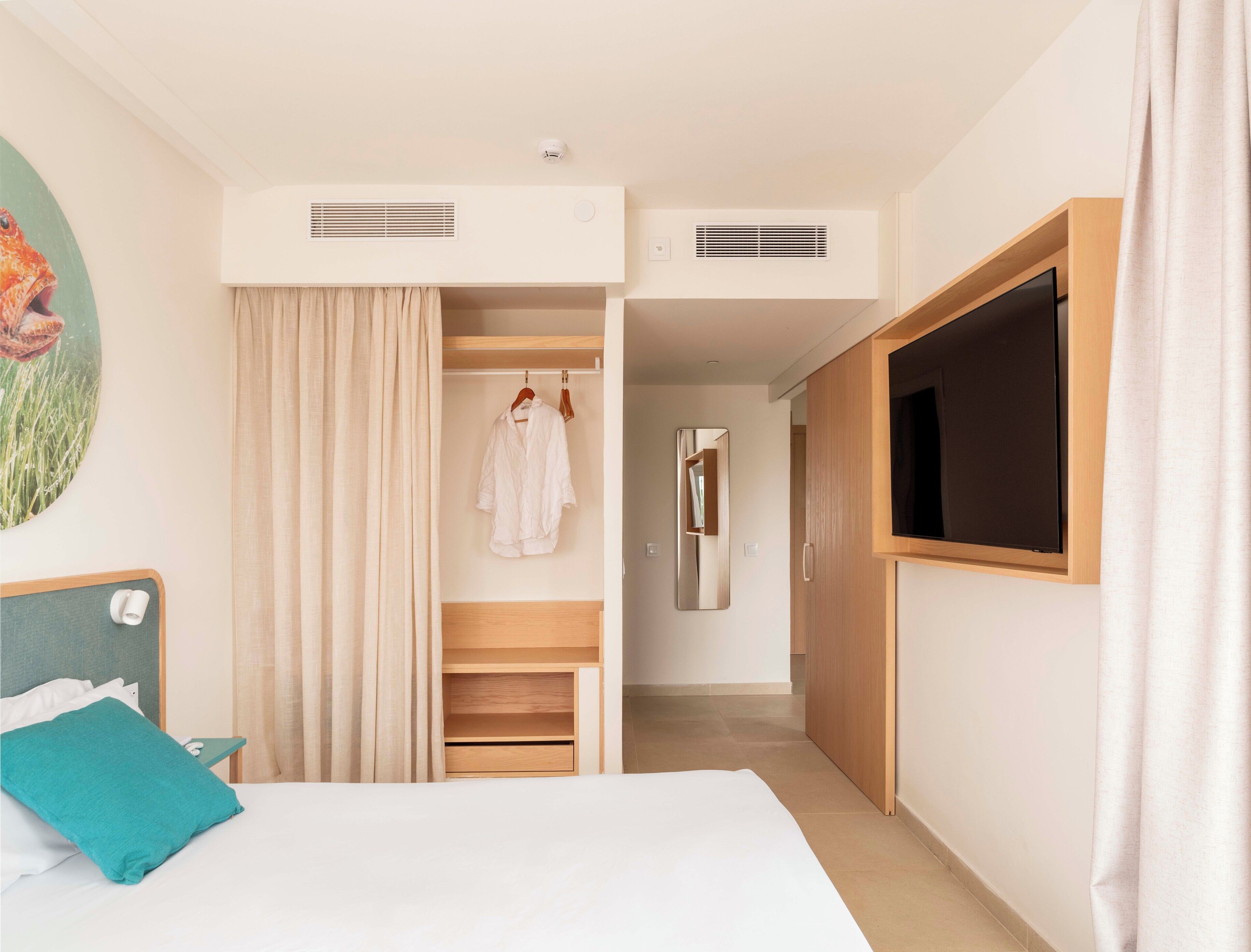 A hotel room with a bed, a TV, a wardrobe, and a bathroom visible through an open door.