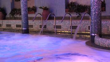 A hot tub area with tiled walls and columns, surrounded by potted plants.