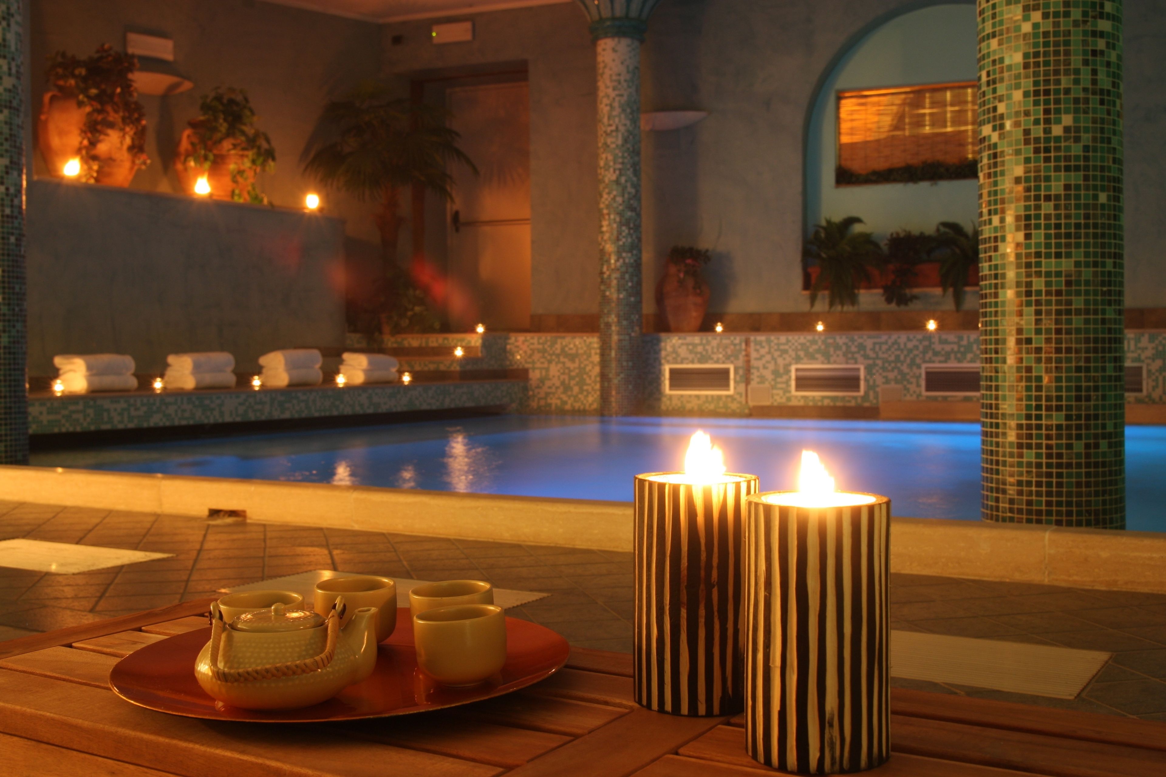A poolside area with candles, a tray of teapots, and a tiled wall.