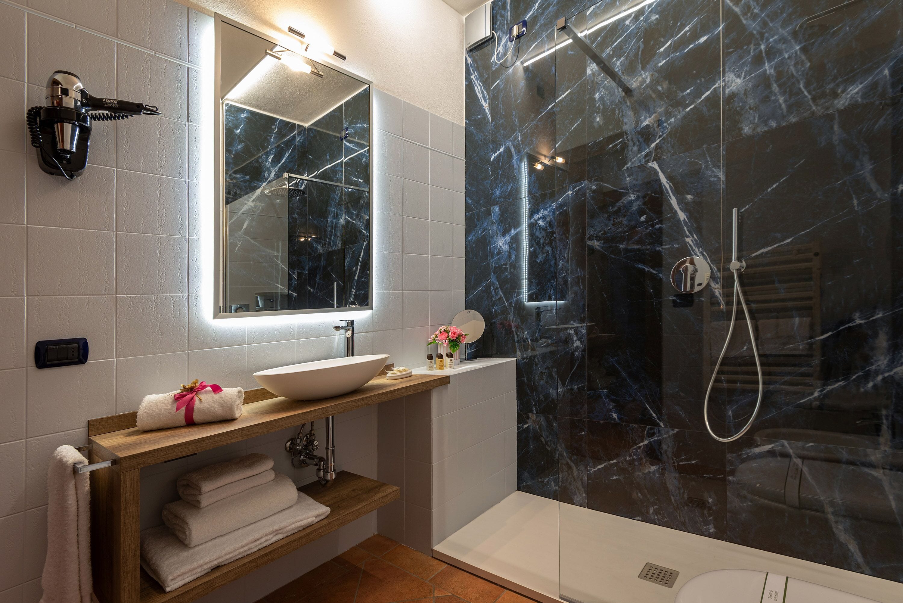 Un baño con pared de ducha de mármol, lavamanos con espejo y toallero con toallas.