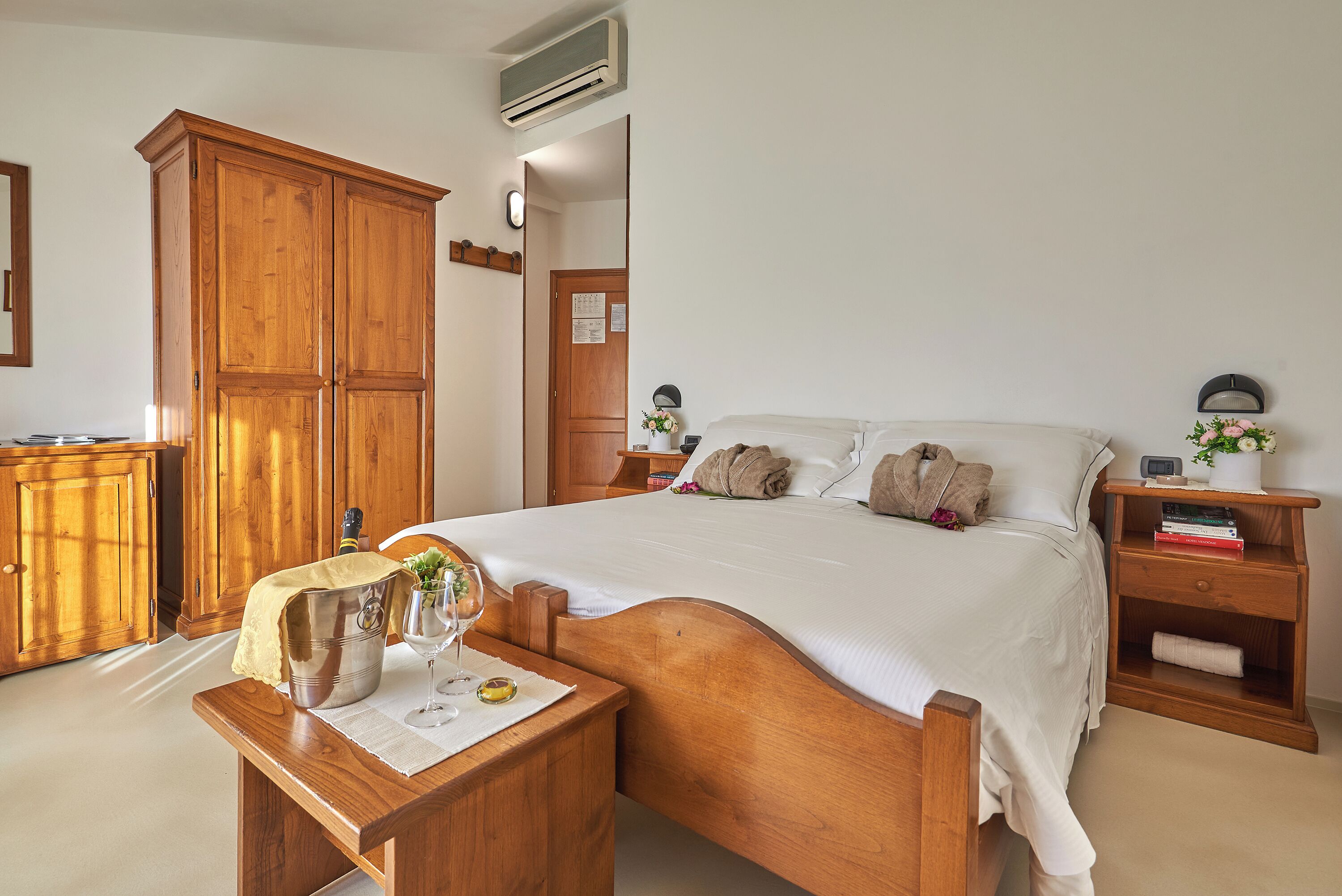 Una camera da letto con un letto in legno, un comodino con una lampada, un armadio in legno e un tavolino con un bicchiere e un boccale.