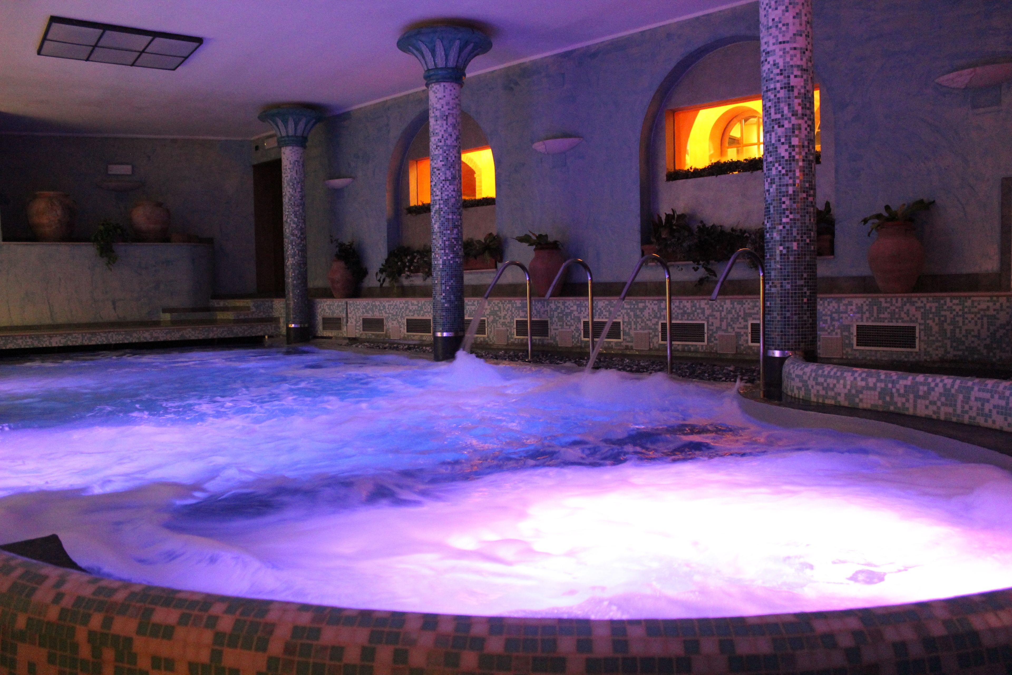 A hot tub area with mosaic tile walls, columns, and potted plants.