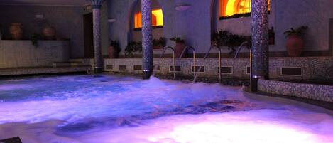 A hot tub area with mosaic tile walls, columns, and potted plants.