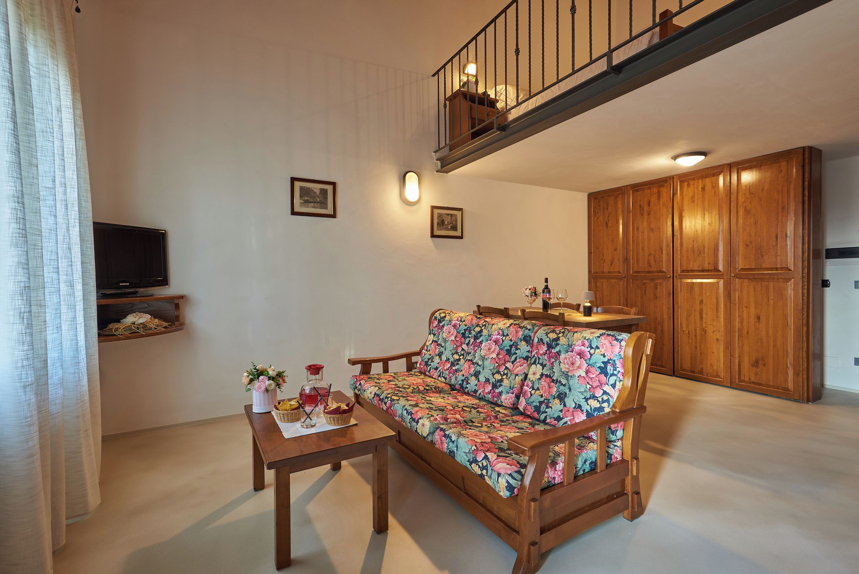 A living room with a wooden sofa, a coffee table, a TV on a shelf, wooden cabinets, and a staircase.