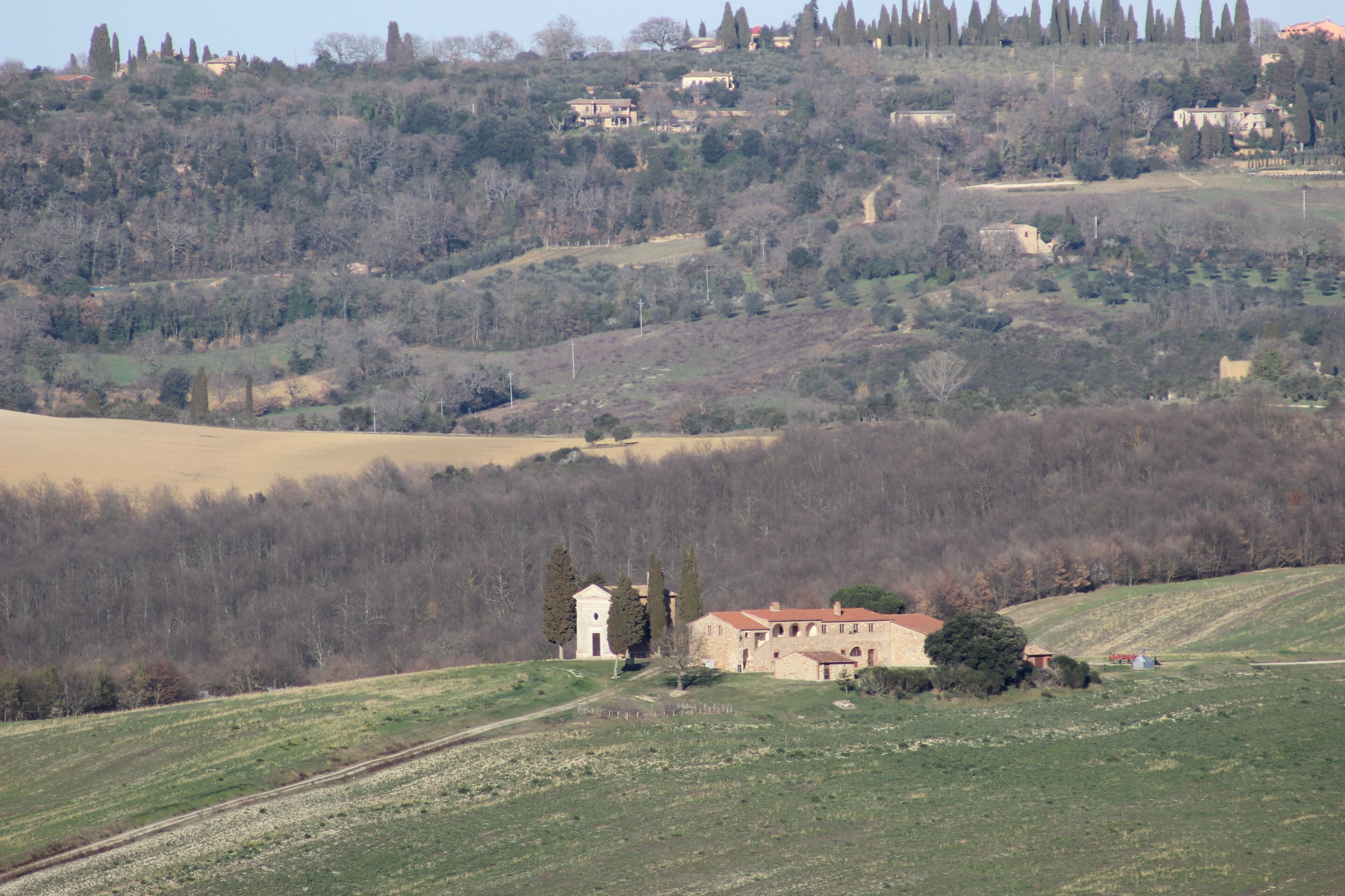 Ländliche Landschaft mit einem Steinhaus, das einen Glockenturm hat, umgeben von Feldern und Bäumen.