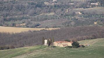 Ländliche Landschaft mit einem Steinhaus, das einen Glockenturm hat, umgeben von Feldern und Bäumen.