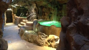 An indoor rock formation with a hot tub and a waterfall feature.