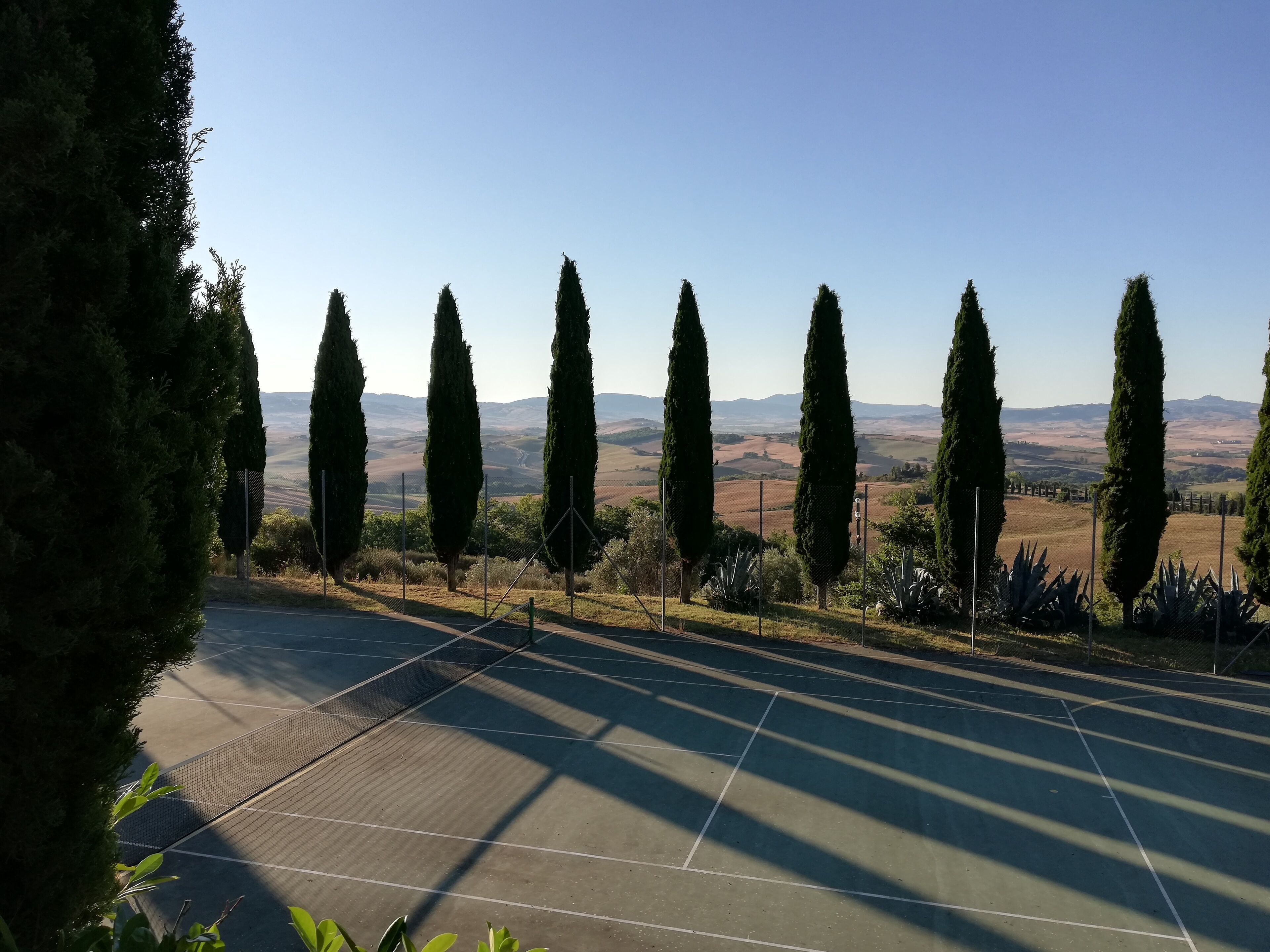 A tennis court with a clear view of distant hills and cypress trees.