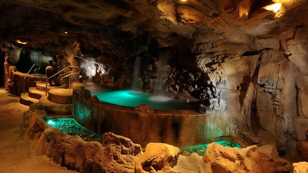 A cave-like interior with a central hot spring, rocky formations, and a staircase leading to a higher level.