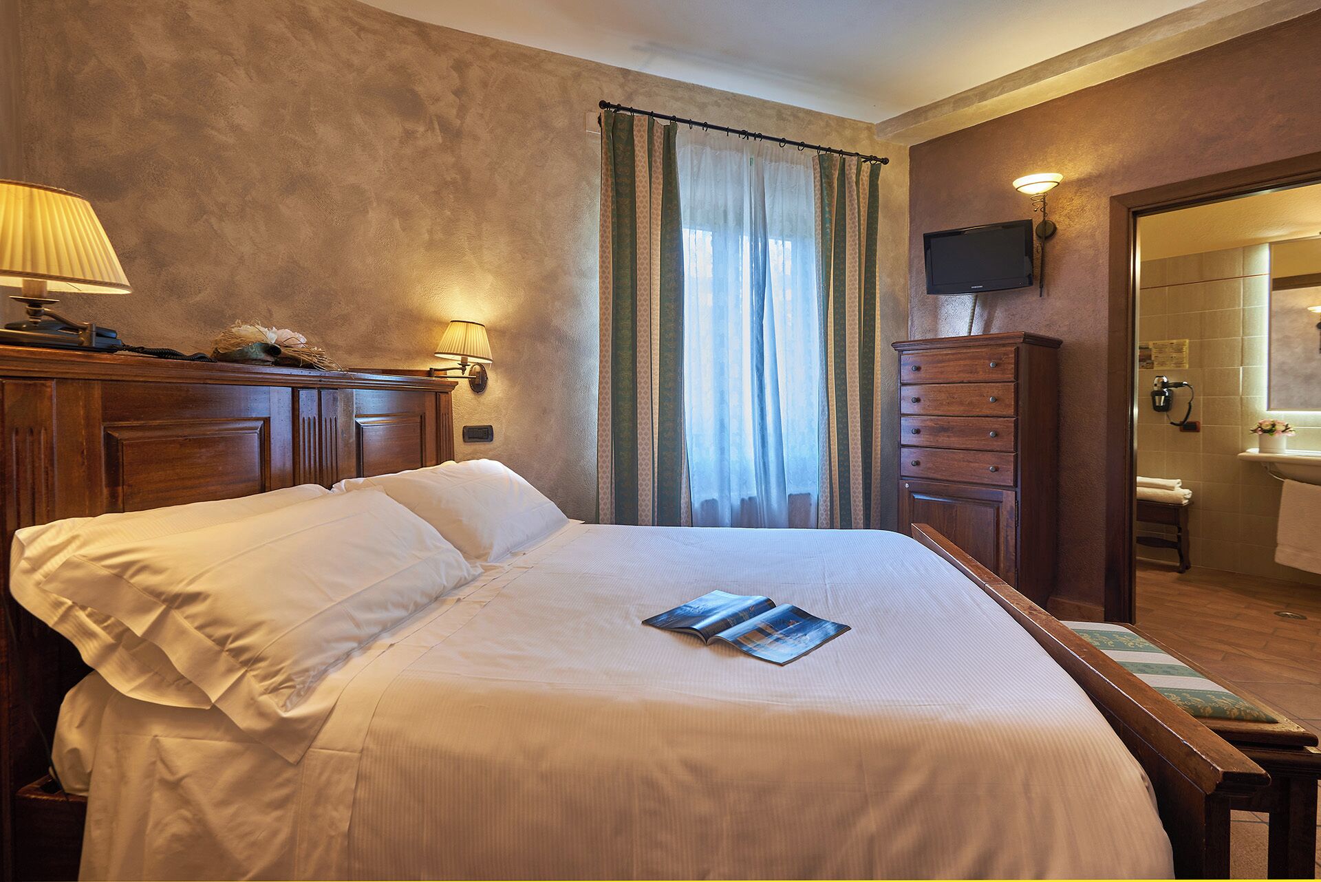 Habitación de hotel con una cama grande, un aparador de madera, un televisor y un baño visible a través de una puerta abierta.