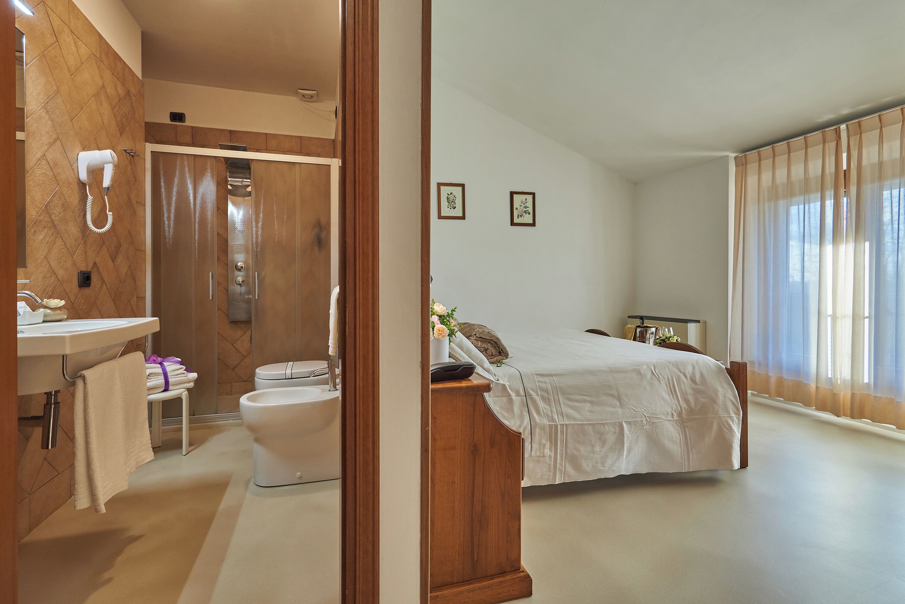 Une salle de bain moderne avec douche, toilettes et lavabo. La pièce adjacente contient un lit avec une tête de lit en bois.