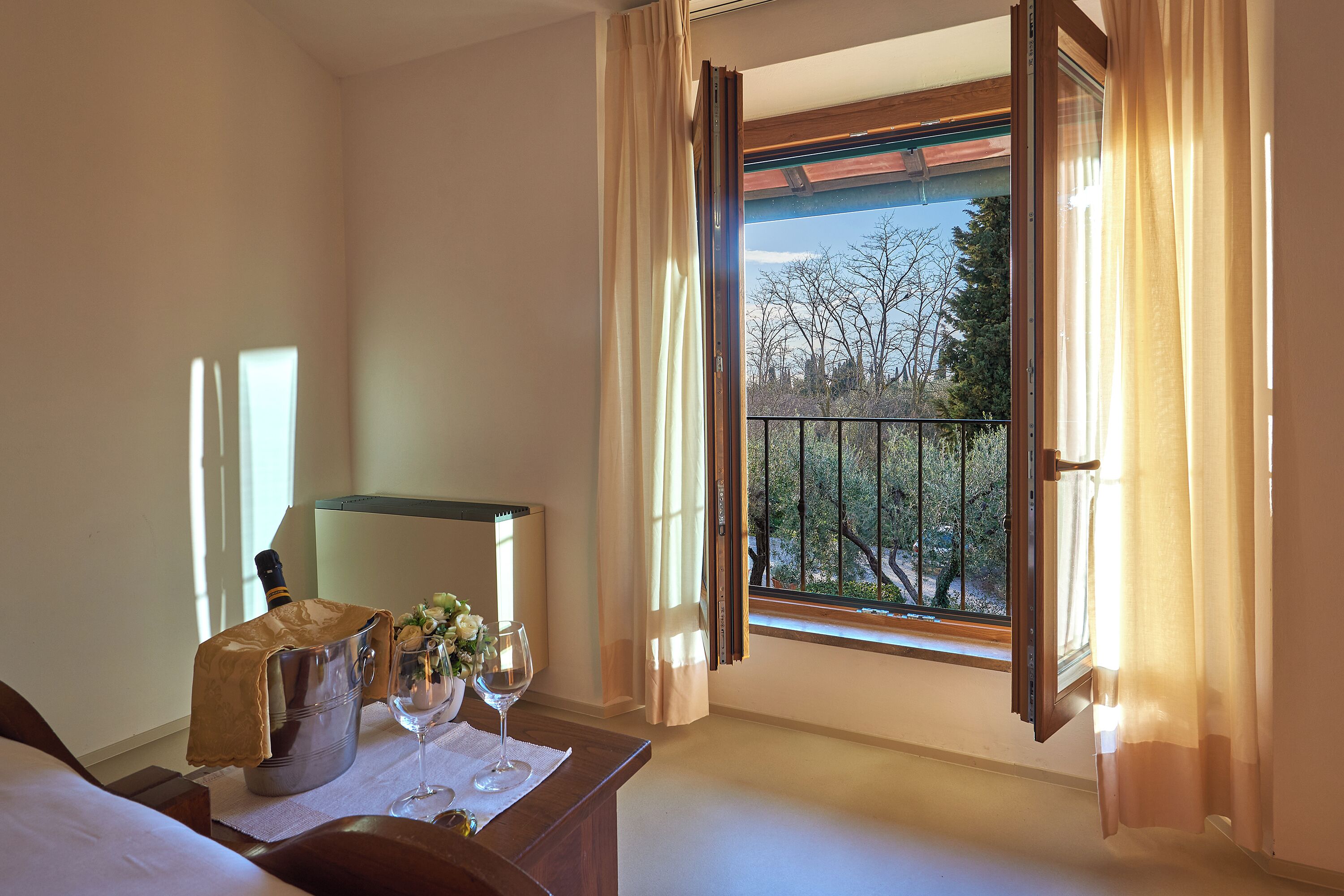 A hotel room with a balcony, a minibar, a bed, and a window with curtains.