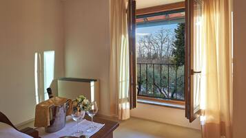 A hotel room with a balcony, a minibar, a bed, and a window with curtains.
