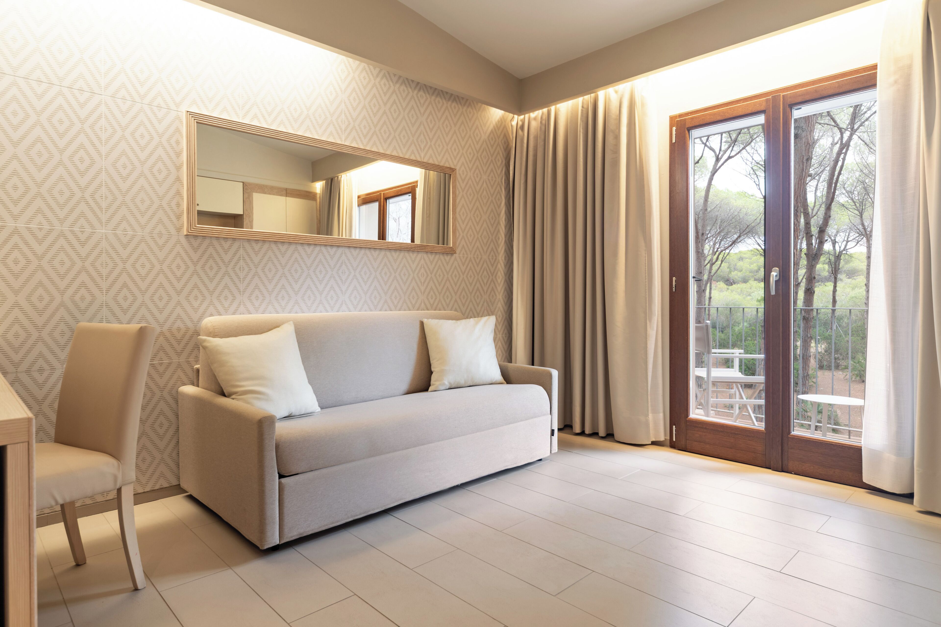 Quarto moderno com sofá, uma cadeira, uma mesa, um espelho e porta de vidro deslizante para área externa.
