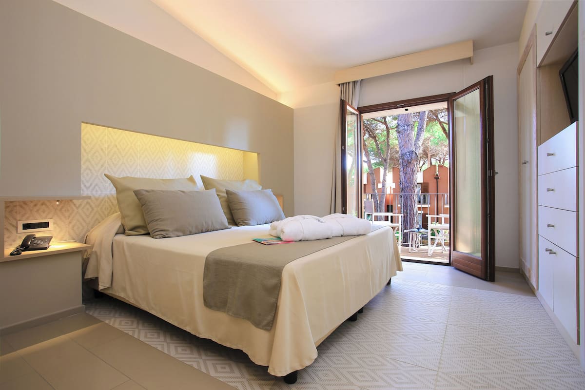 A bedroom with a bed, bedside table, and a view of the outside.