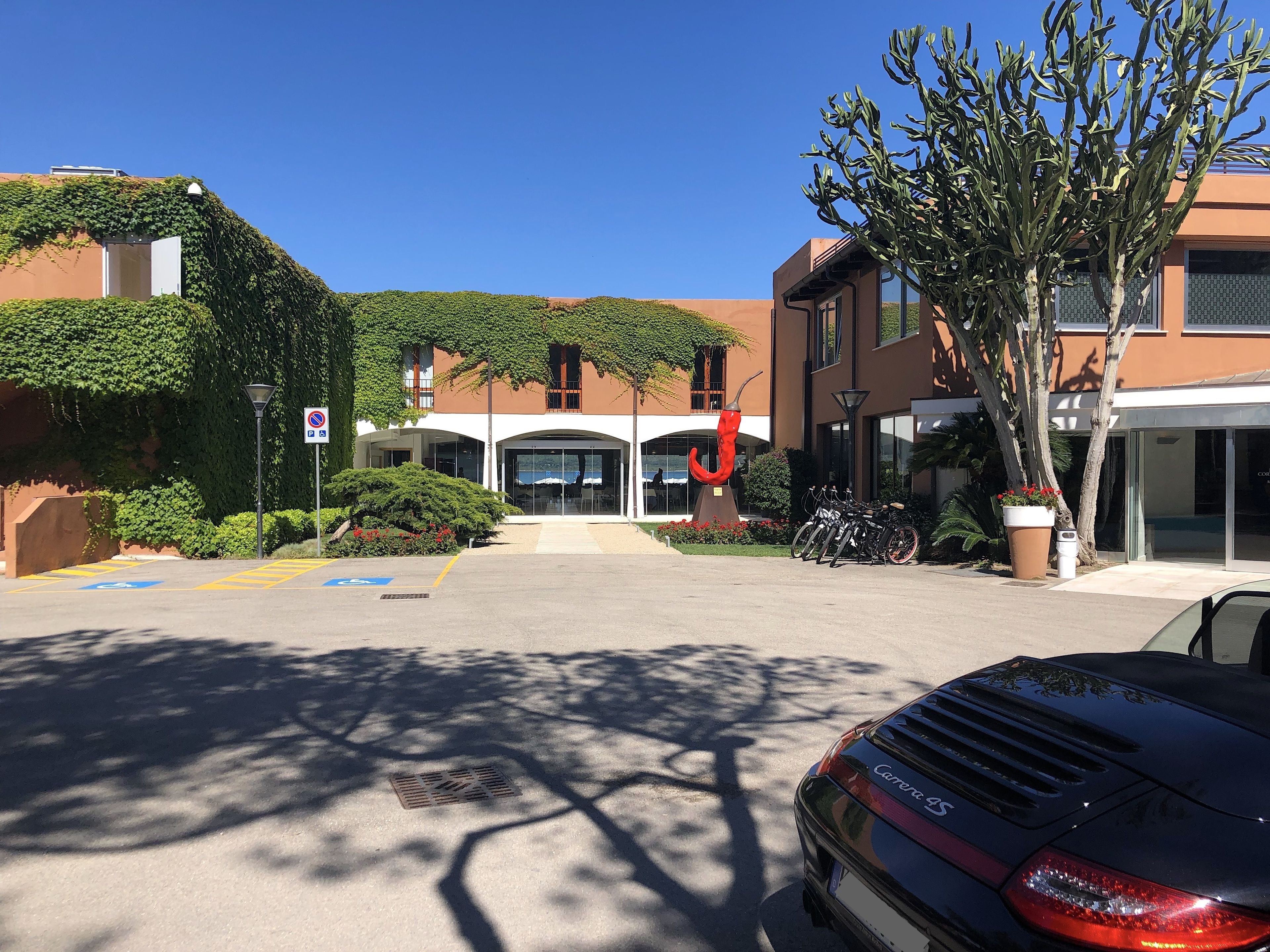 Un edificio de diseño moderno, con un amplio acceso con puertas de vidrio, una zona de estacionamiento con bicicletas y una escultura roja.