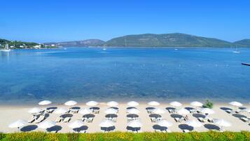 Une plage avec une eau d’un bleu limpide, des parasols blancs et des chaises longues disposées en rangées.