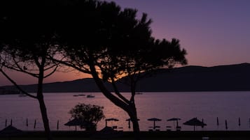 Scena di spiaggia con tramonto, alberi e ombrelloni.
