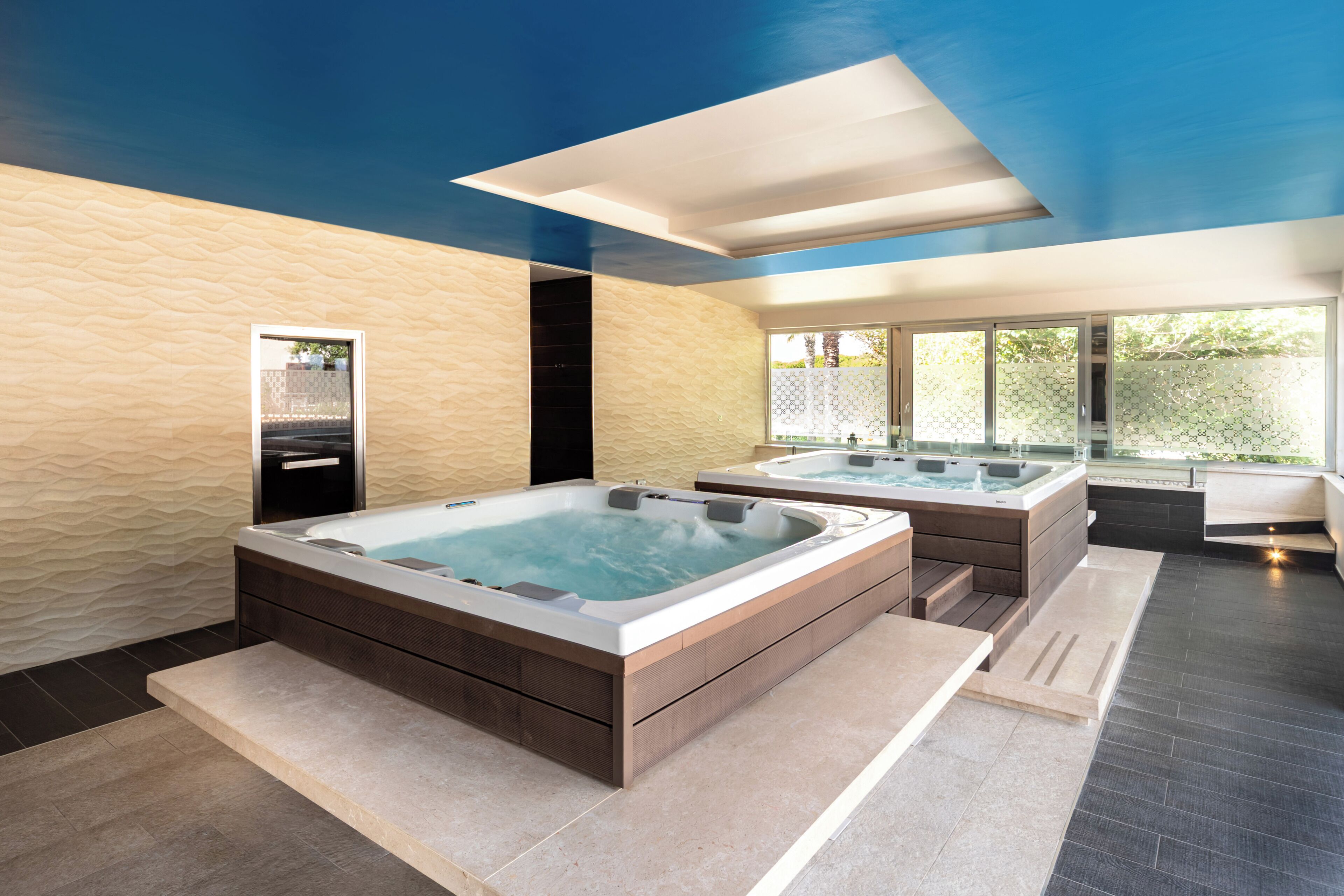 A modern spa area with two hot tubs, a large window, and a textured wall.