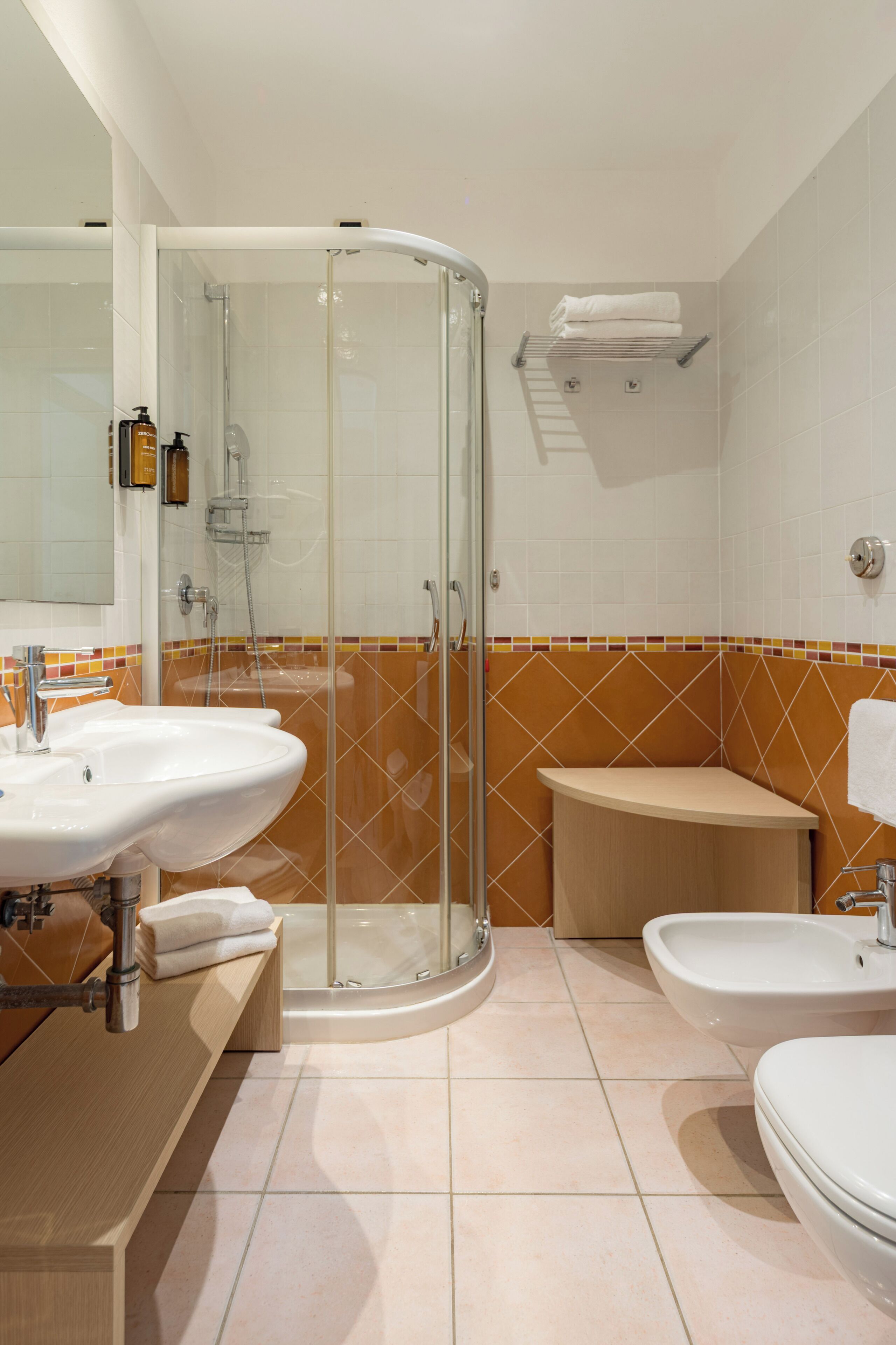 A modern bathroom with a glass-enclosed shower, two sinks, a bidet, and a toilet.