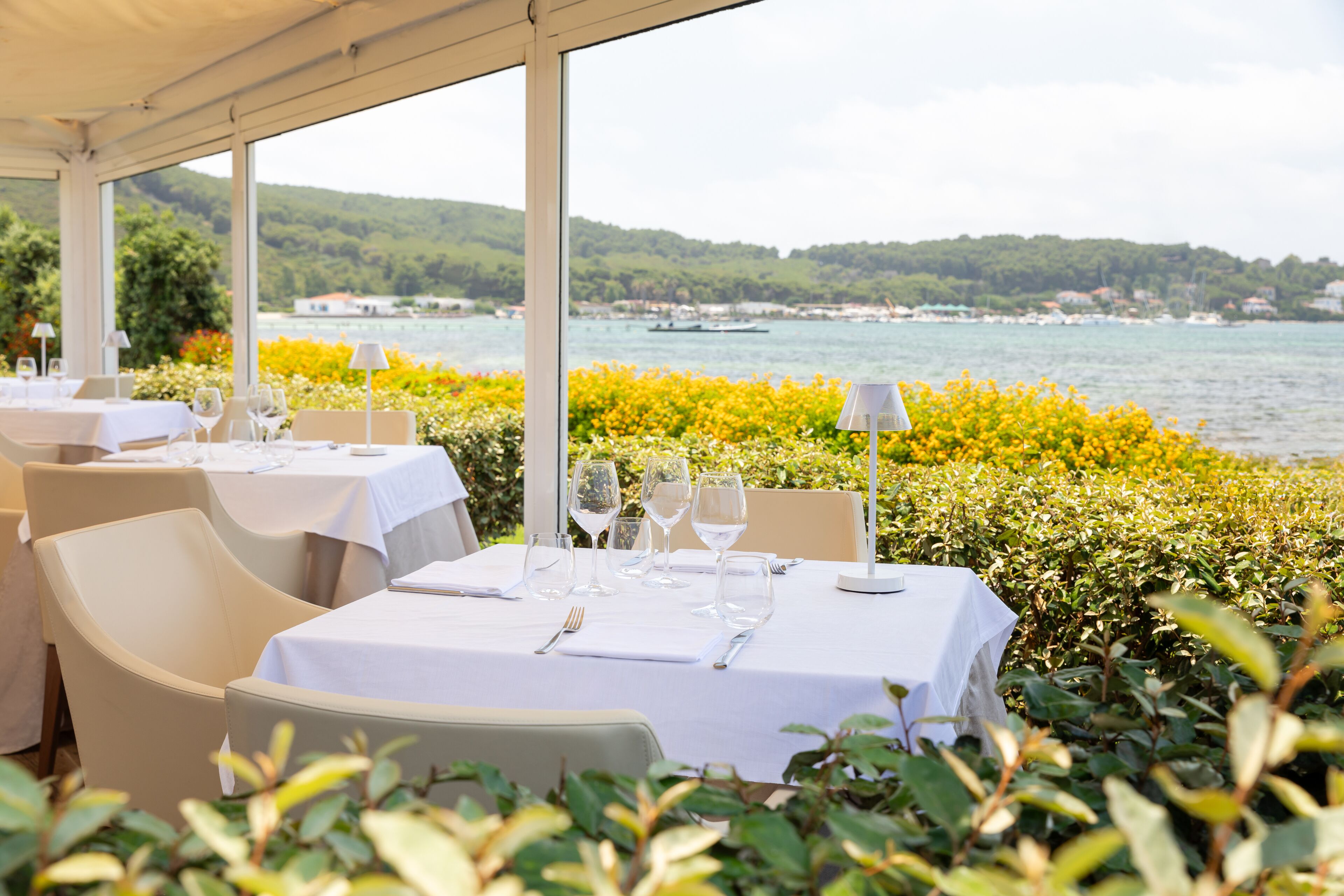 An outdoor dining area with tables set for a meal, overlooking a body of water and a hillside.