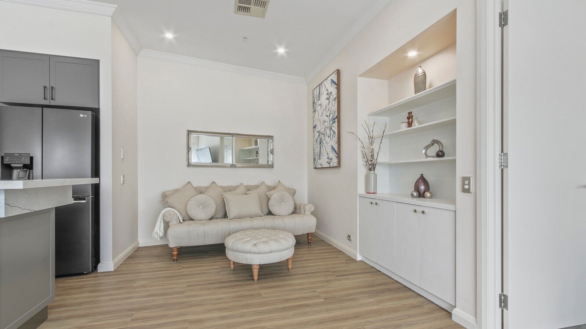 Una sala moderna con un sofá gris, un reposapiés a juego y un mueble blanco con objetos decorativos.