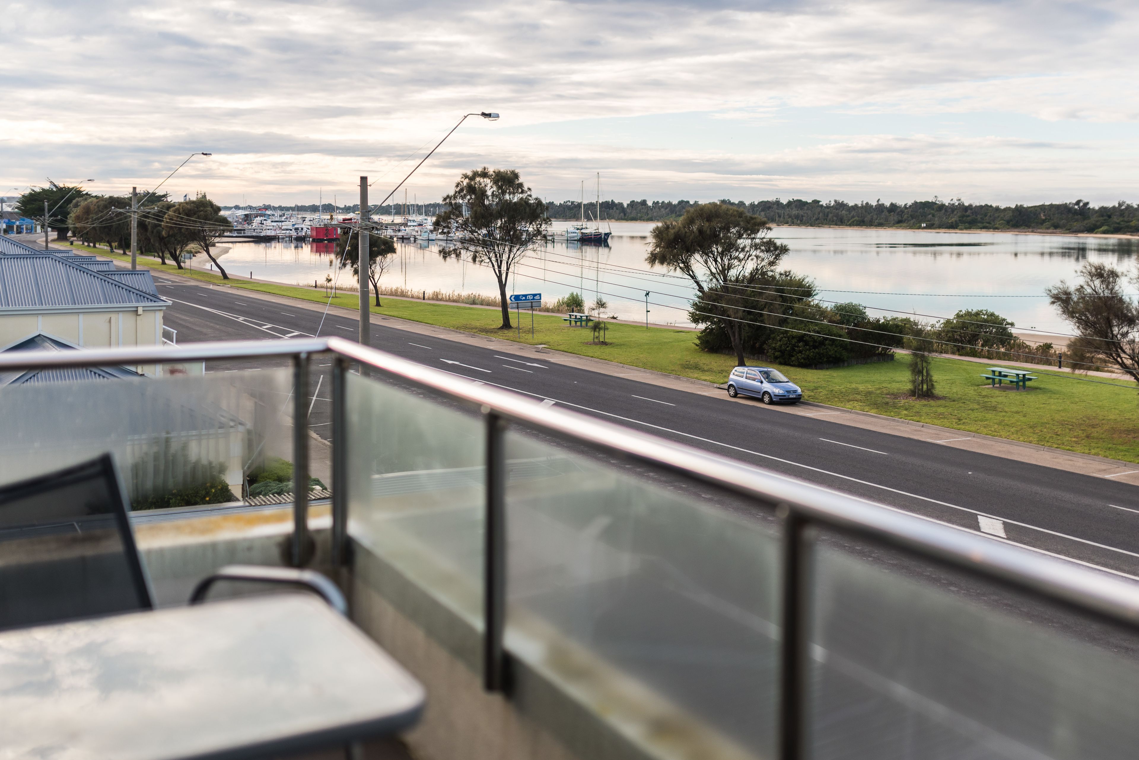 A view from a balcony overlooking a road with a body of water and boats in the background.