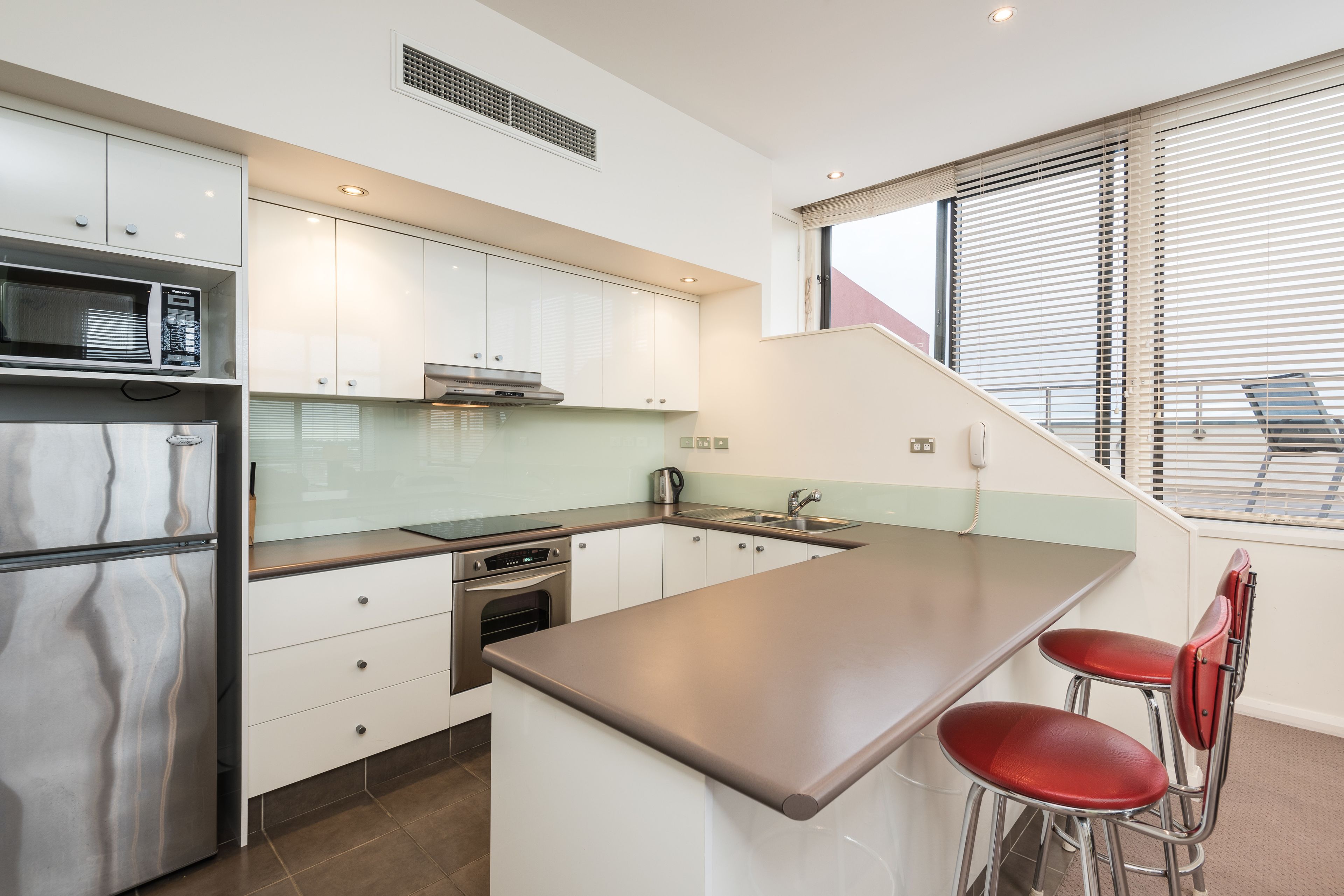 A modern kitchen with white cabinets, stainless steel appliances, and a large island with two red bar stools.
