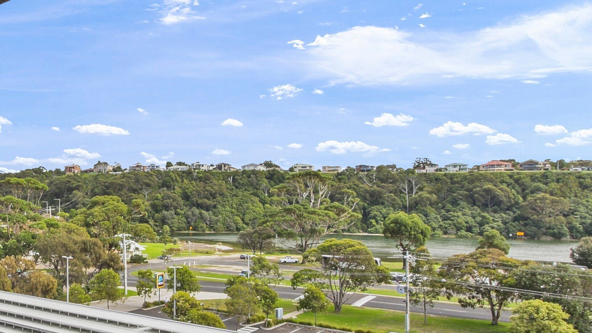 A coastal landscape with a road, greenery, and buildings on a hill.