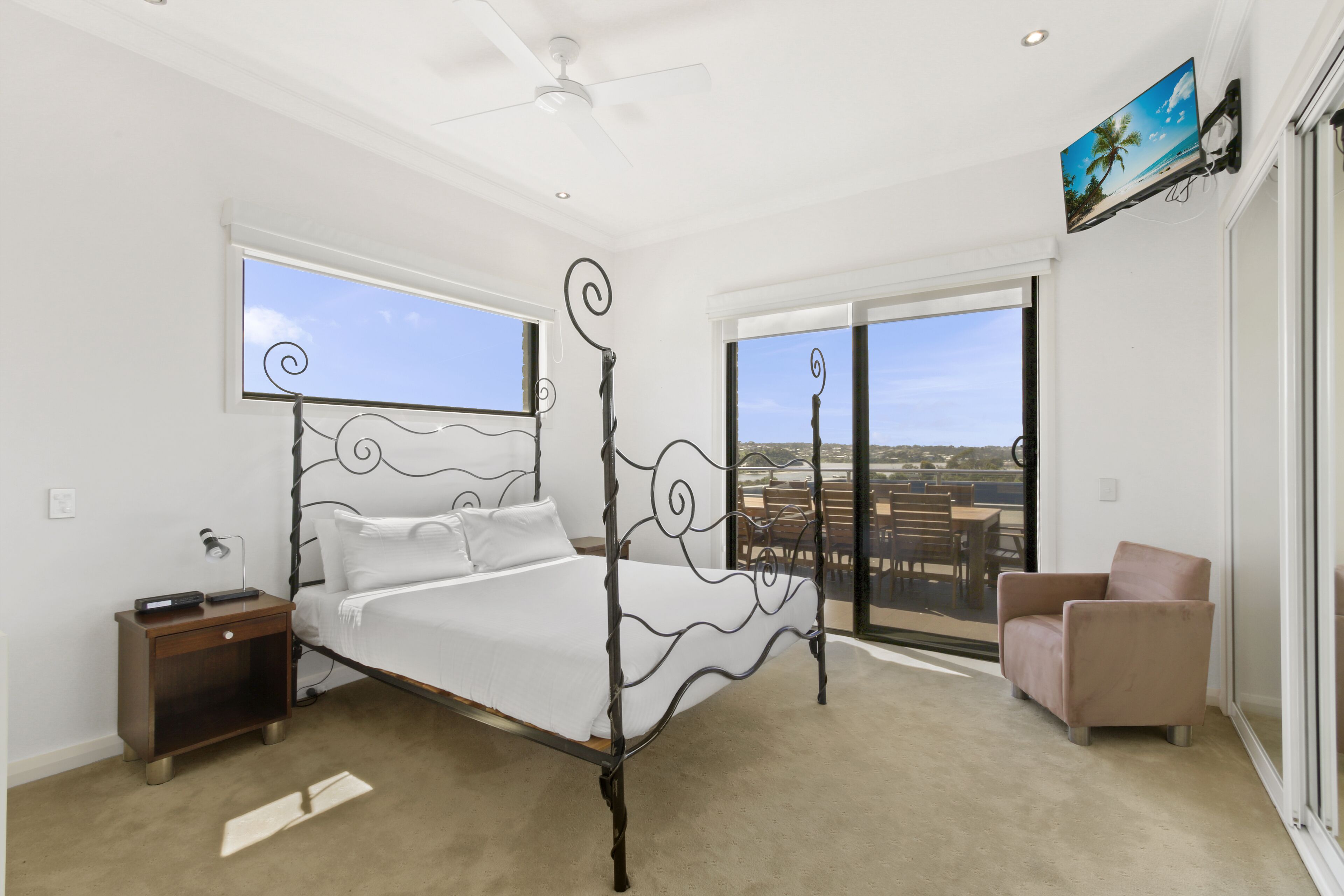 A bedroom with a four-poster bed, a nightstand, a chair, and a TV on the wall.